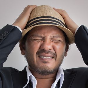 Man wearing a hat to hide hair loss, showing emotional stress caused by male pattern baldness