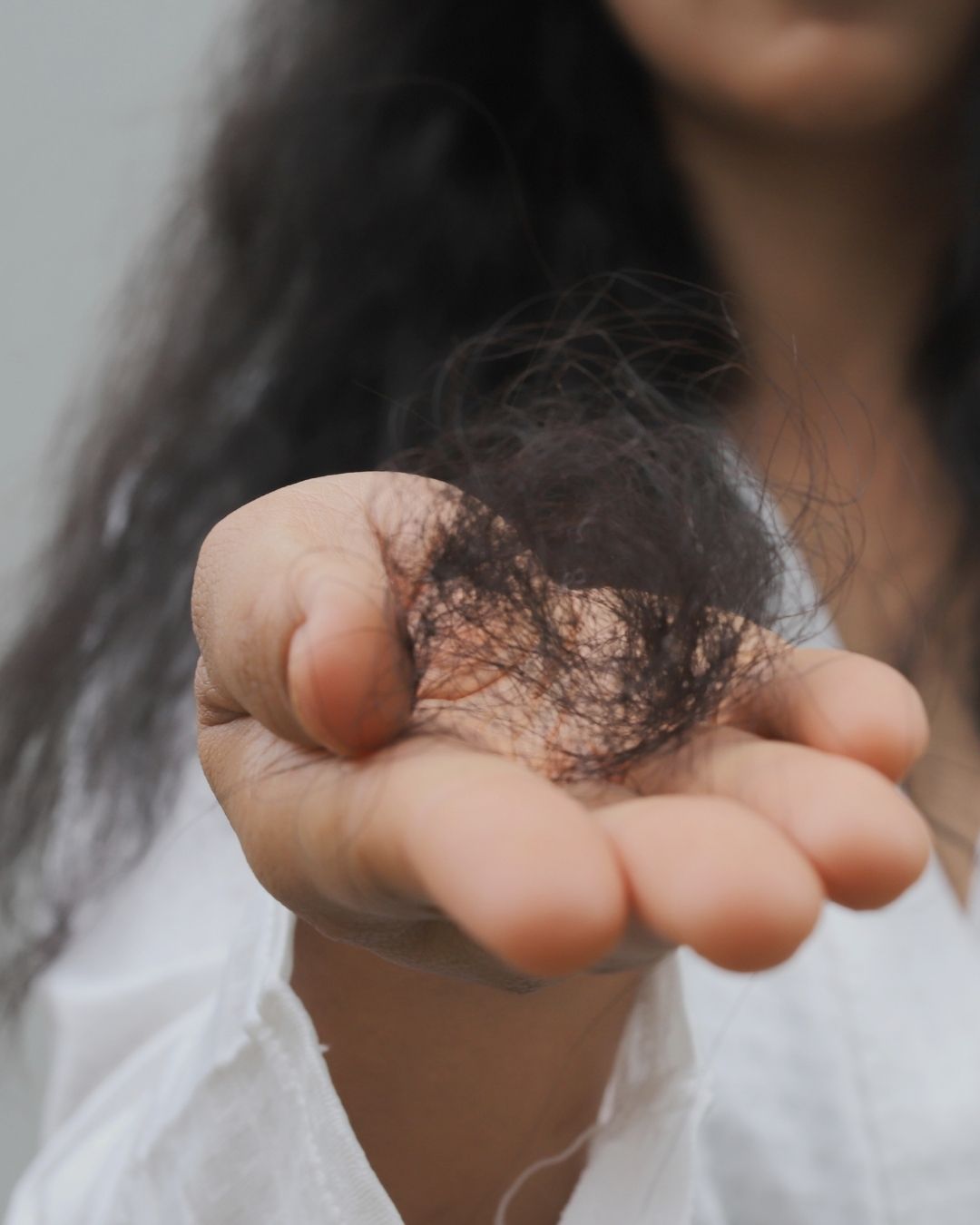 "Person experiencing hair fall, feeling that each strand lost represents a part of their identity."